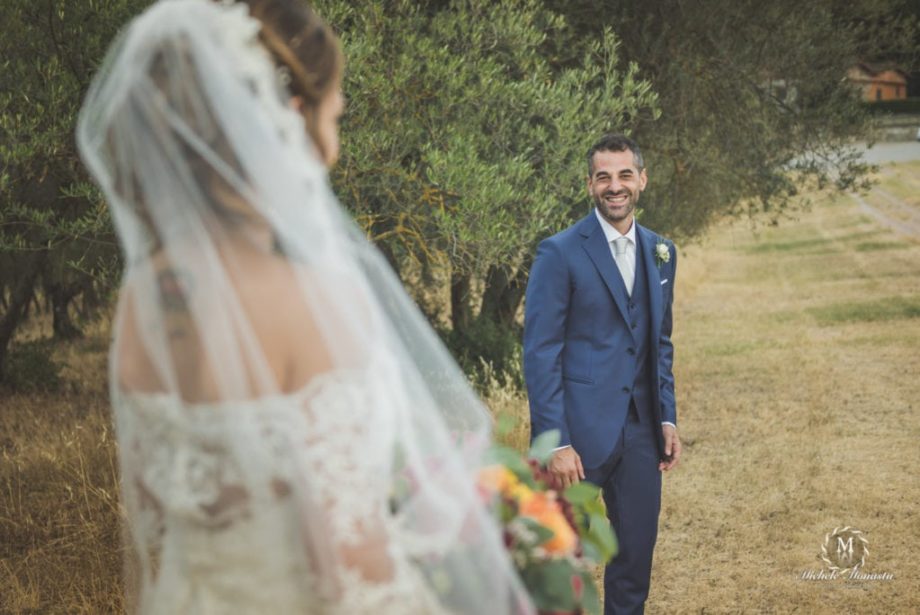 sposo sorride alla sposa in un campo di ulivi toscani